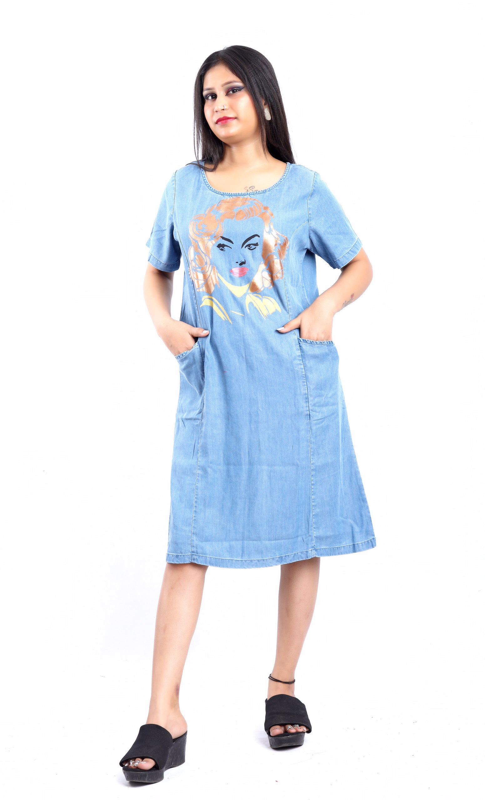 Woman wearing a casual denim midi dress with graphic print standing with hands in pockets midi with jeans