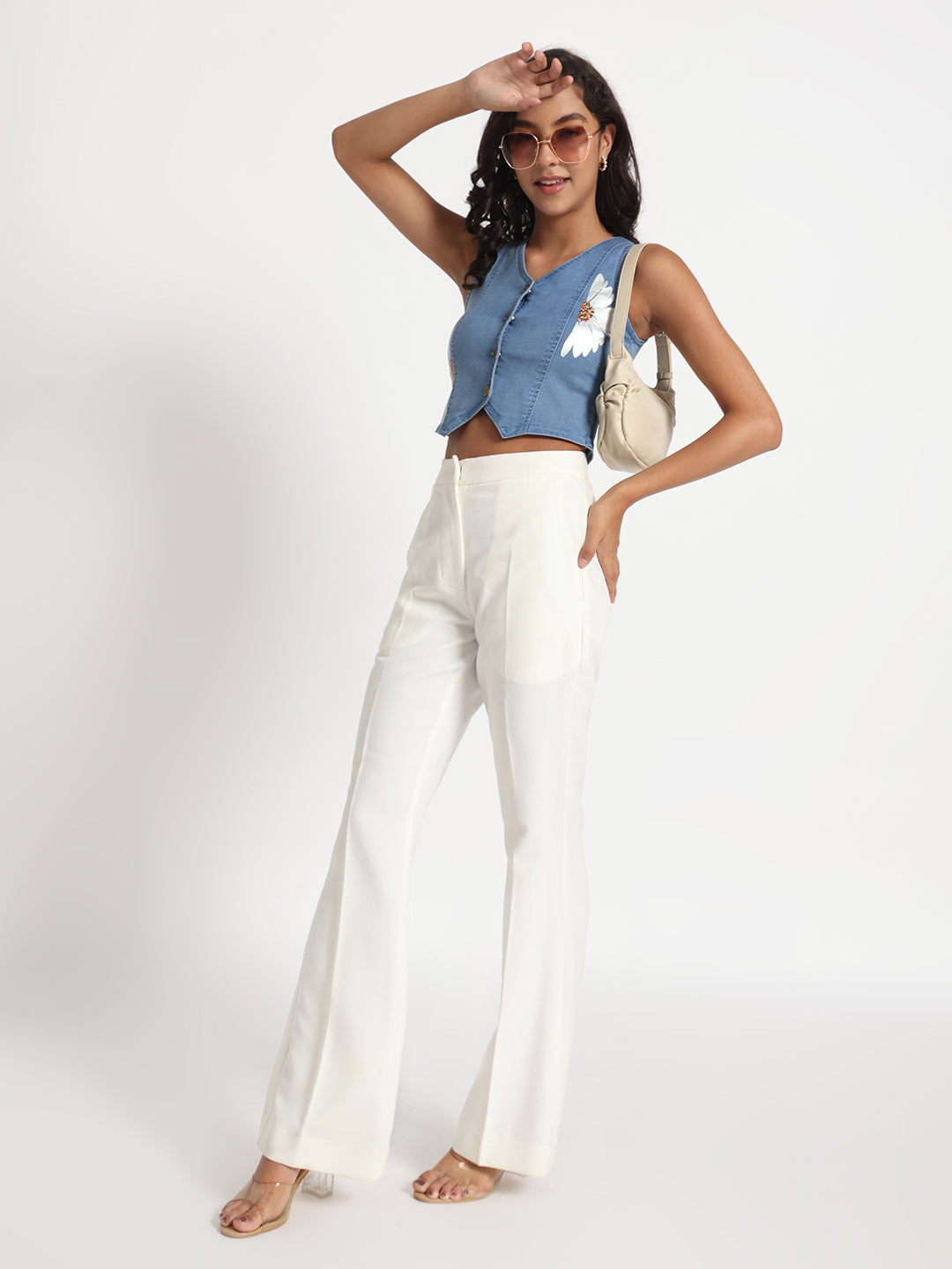 Woman wearing a sleeveless top in jeans with button details paired with white wide-leg pants and sunglasses