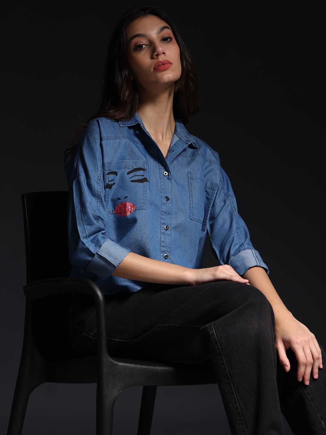 Gotamoda top jeans shirt with artistic face print worn by woman sitting on black chair