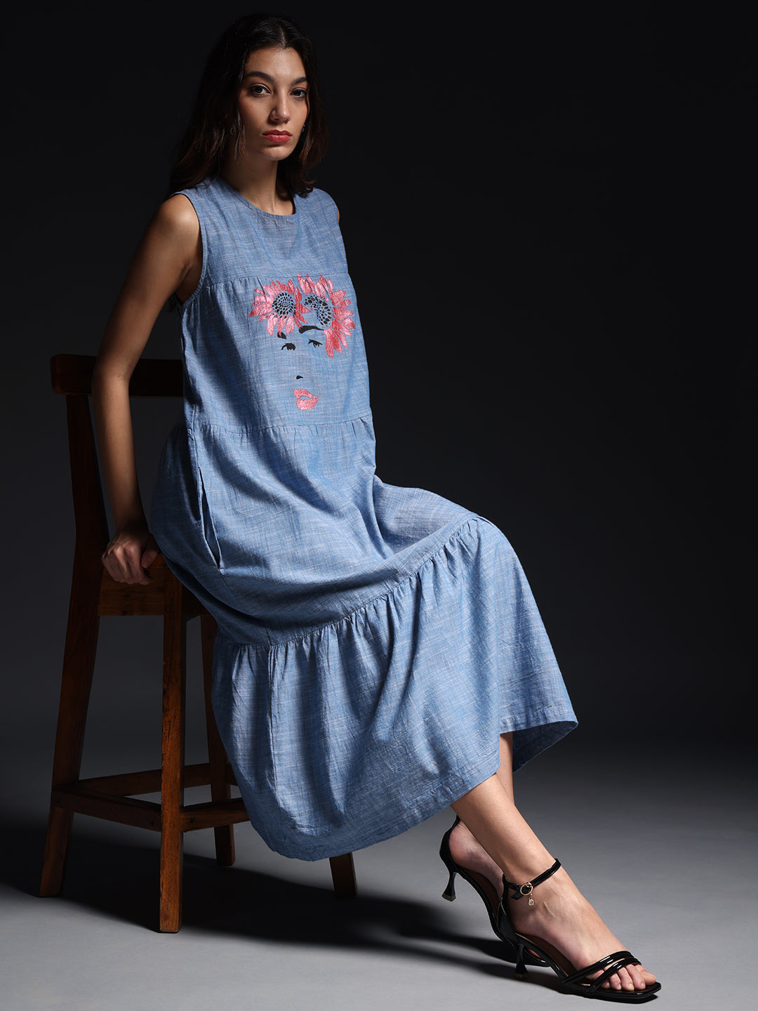 Woman wearing Comfortable Hand Painted denim Dress with floral face design sitting on wooden chair