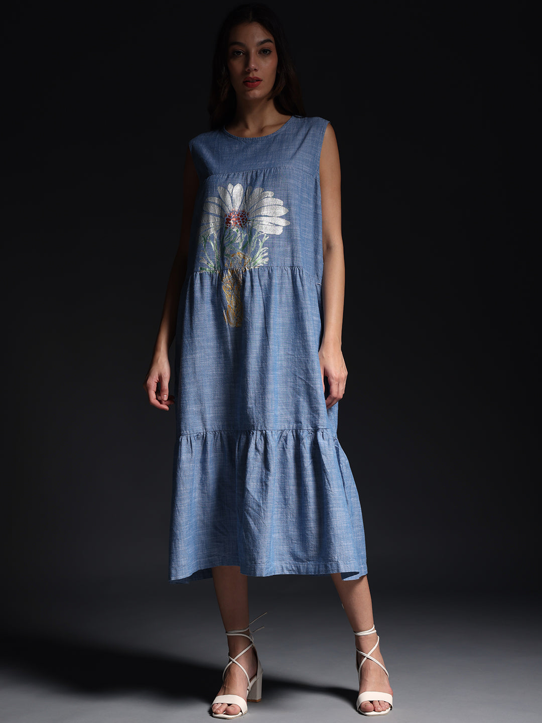 Woman wearing a blue sleeveless summer maxi dress with floral print and white sandals