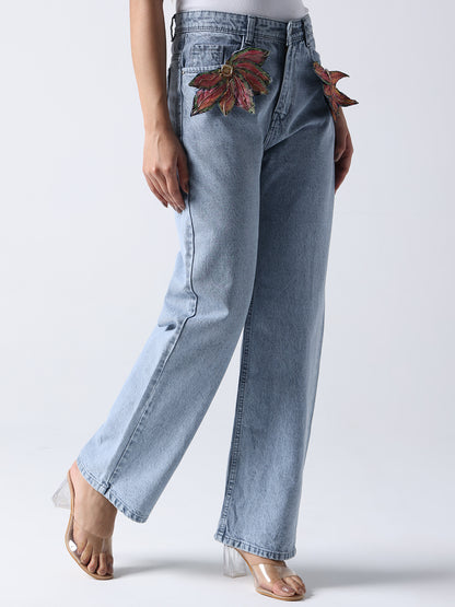 Light wash jeans featuring decorative brooch on jeans styled as red and green leaves near the pockets
