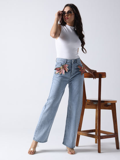 Woman wearing light blue jeans with floral brooch on jeans paired with white sleeveless top and sunglasses