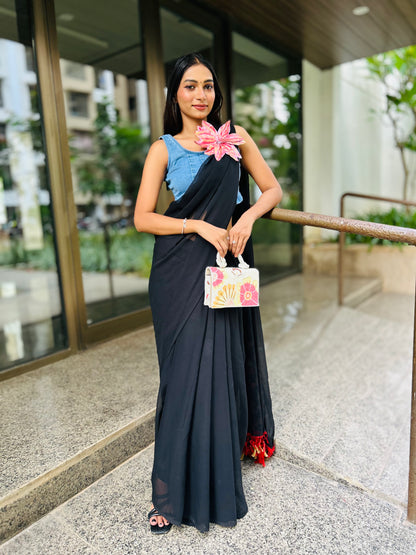 Woman wearing black saree with denim blossom brooch and blue blouse holding floral handbag outdoors