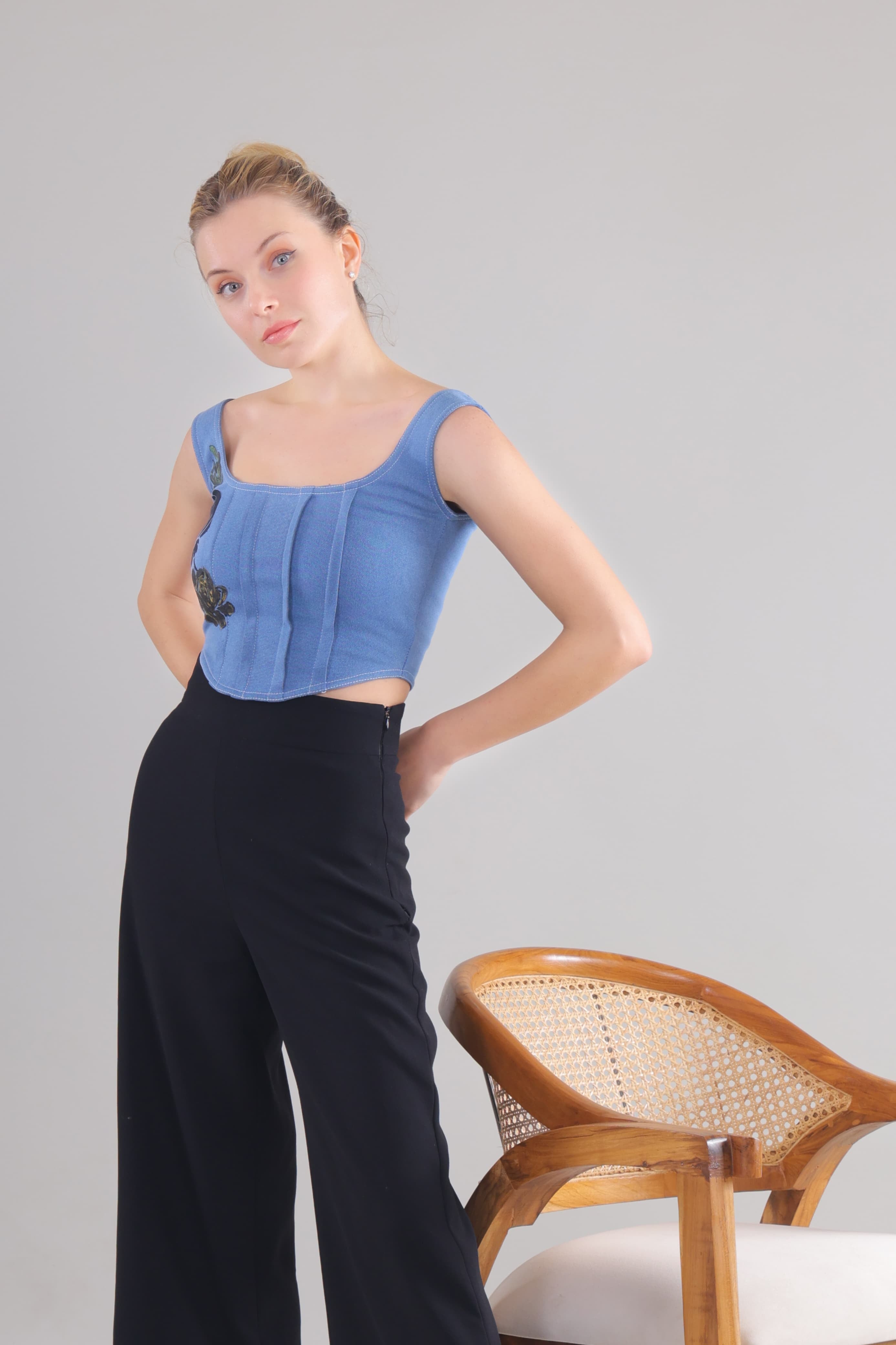 Gotamoda Denim Corset Top worn by model paired with black high-waisted pants and wooden chair nearby