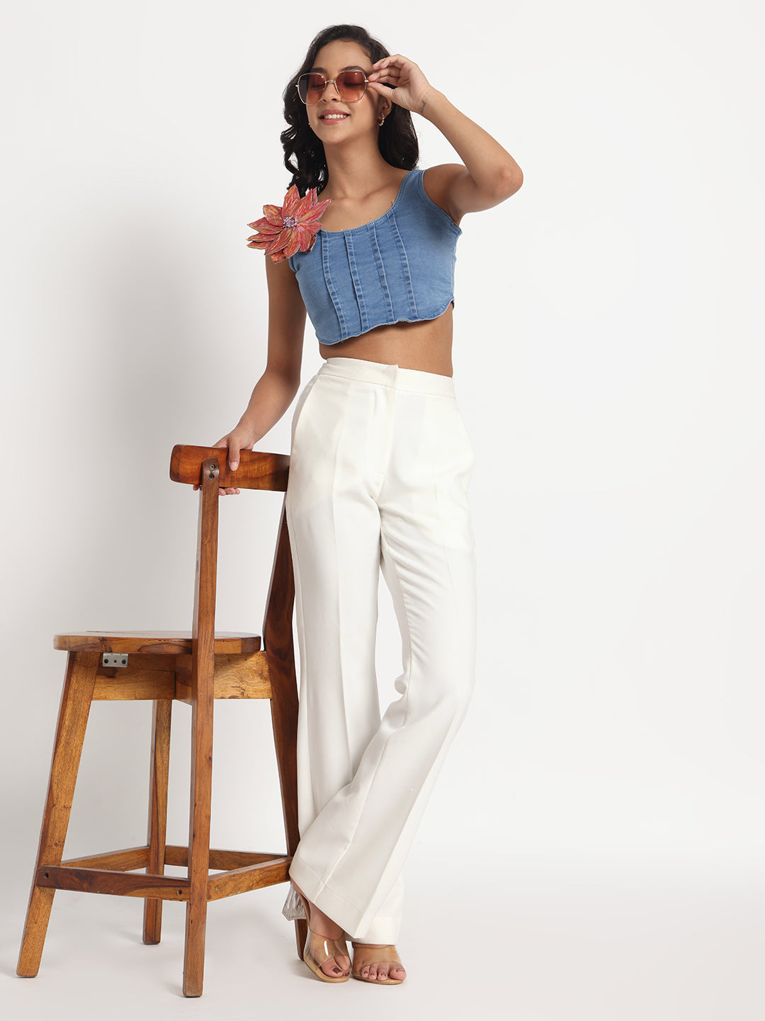Woman wearing Gotamoda blue jeans top with a flower detail paired with white wide-leg pants