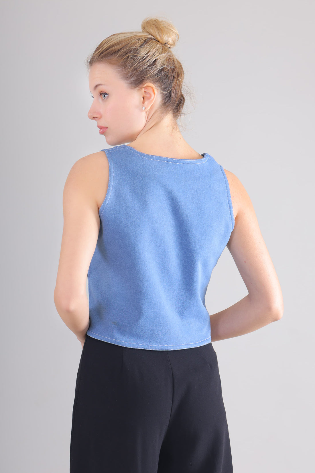Back view of woman wearing light blue sleeveless jeans Top paired with black pants