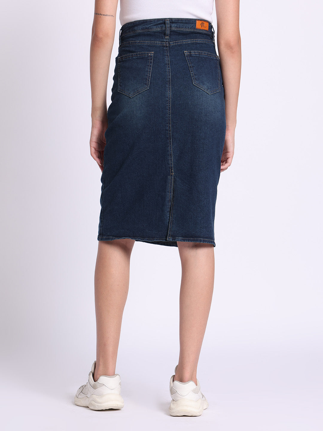 Back view of woman wearing dark blue denim skirt paired with white sneakers and white top