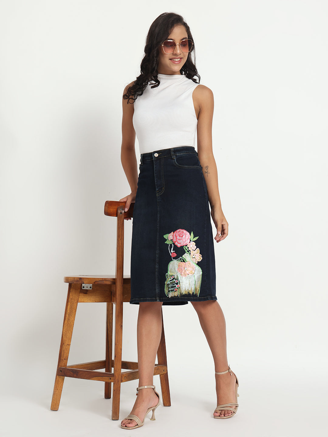 Gotamoda hand-painted denim skirt with floral and abstract art worn by woman in white sleeveless top and heels