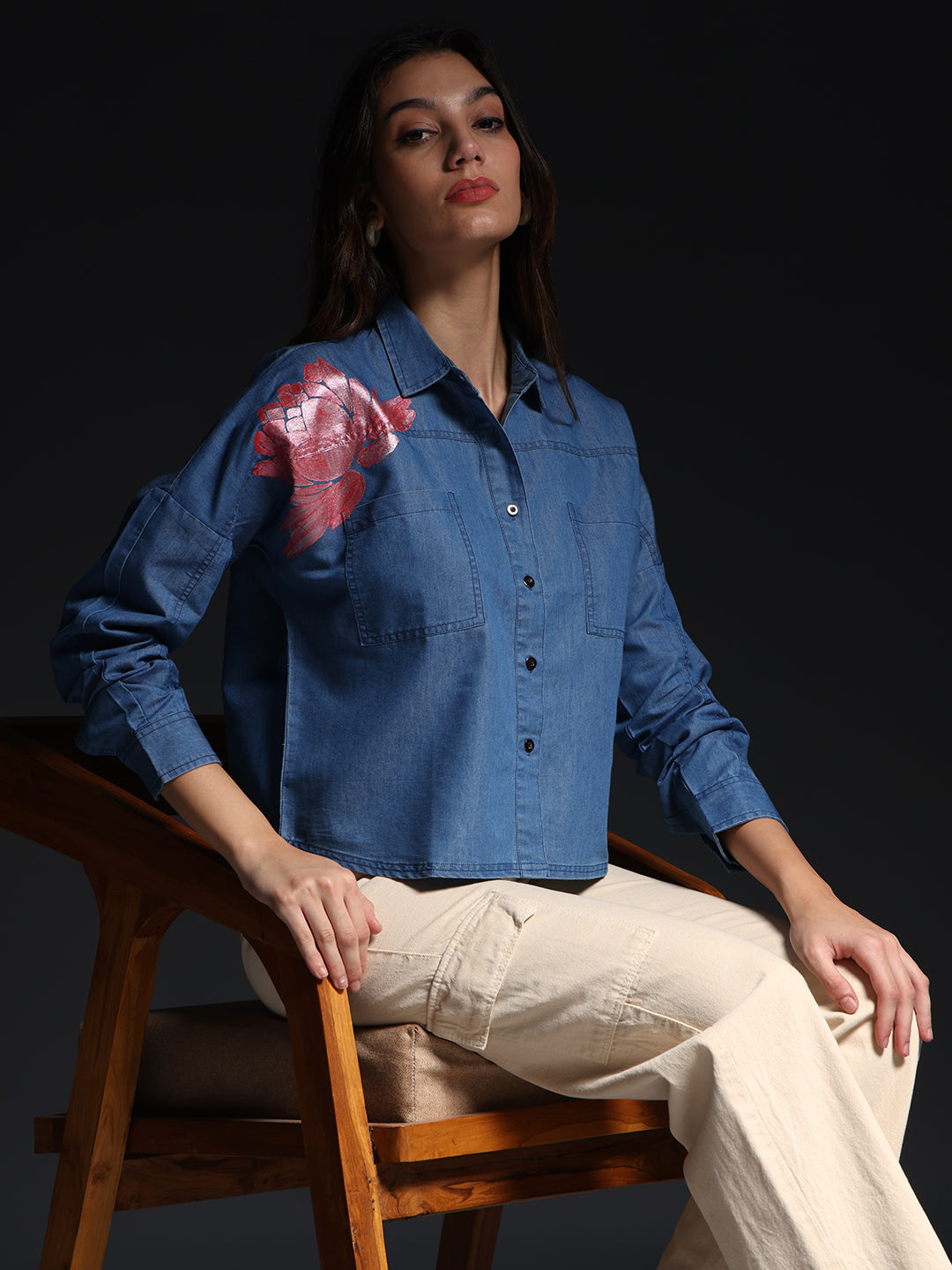 Gotamoda top jeans shirt with button-up front and pink floral detail on shoulder worn by woman sitting on wooden chair