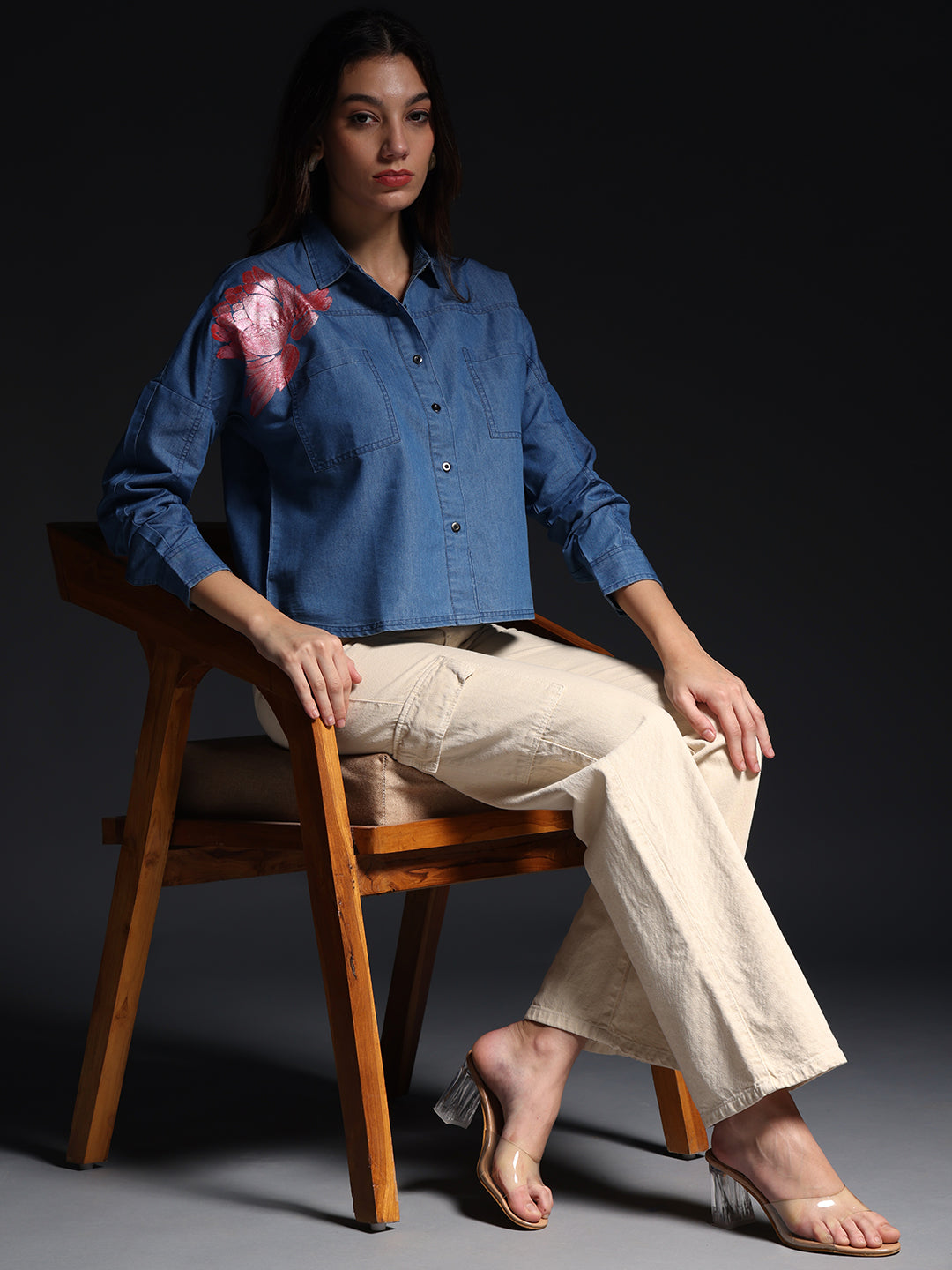Gotamoda top jeans shirt with floral detail on shoulder worn by model sitting on wooden chair