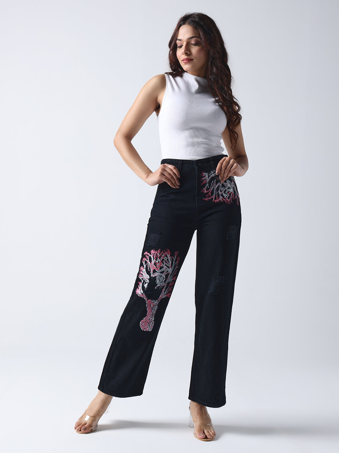 Woman wearing Gotamoda hand painted jeans with floral and tree designs paired with a white sleeveless top