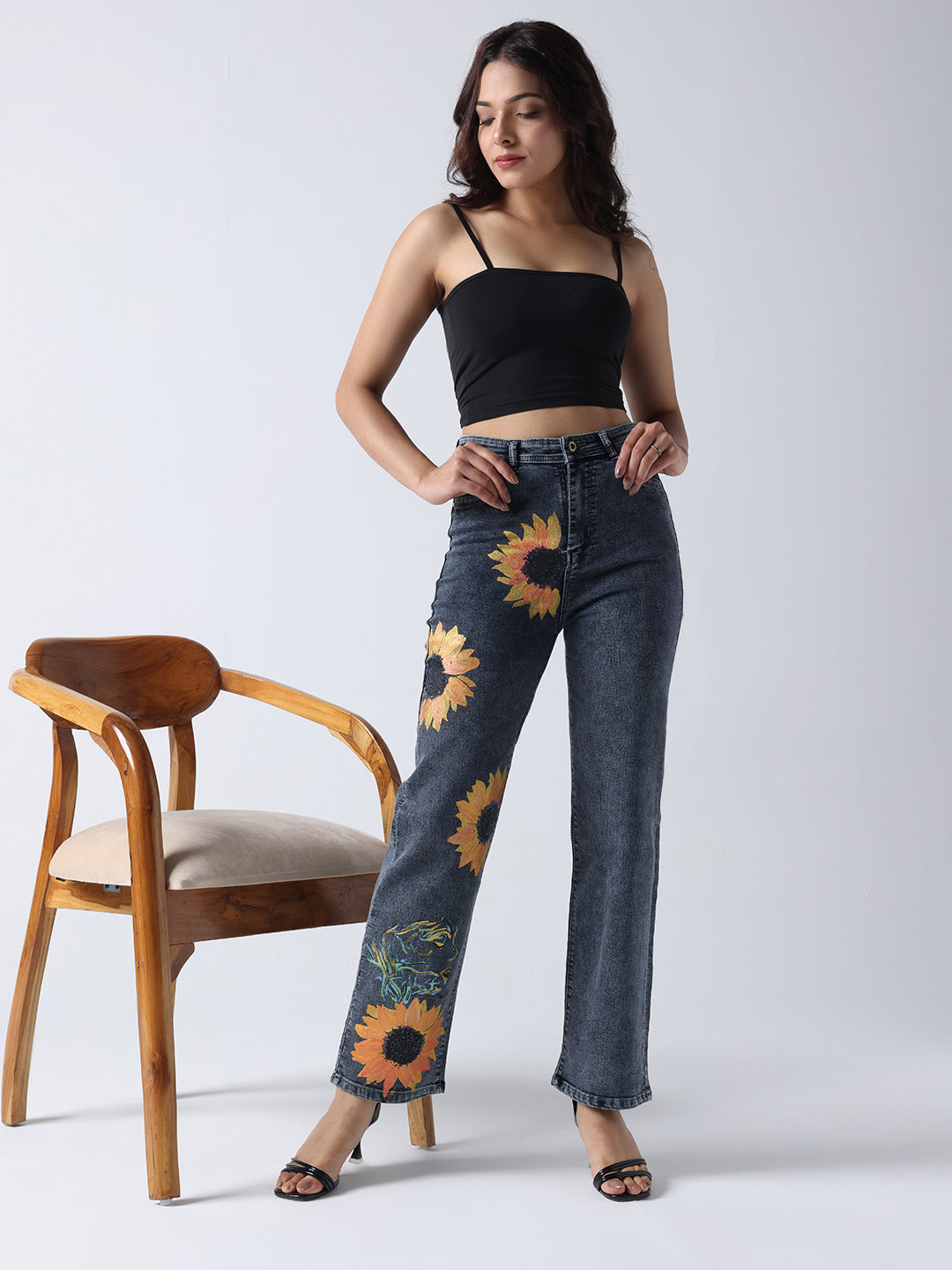 Gotamoda woman wearing black crop top and hand painted jeans with sunflower design standing next to wooden chair