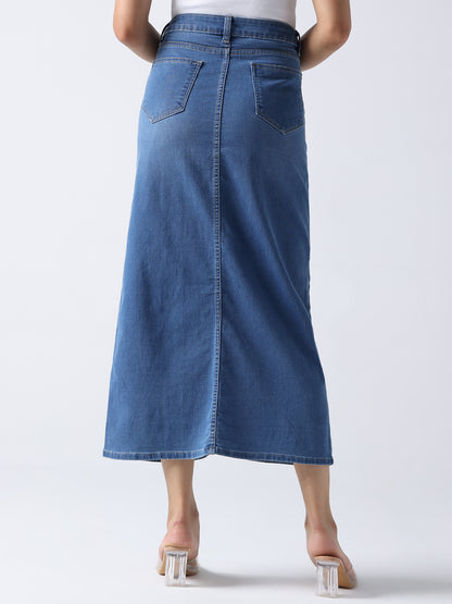 Back view of queen bee denim midi skirt in blue worn by model with white top and clear heels