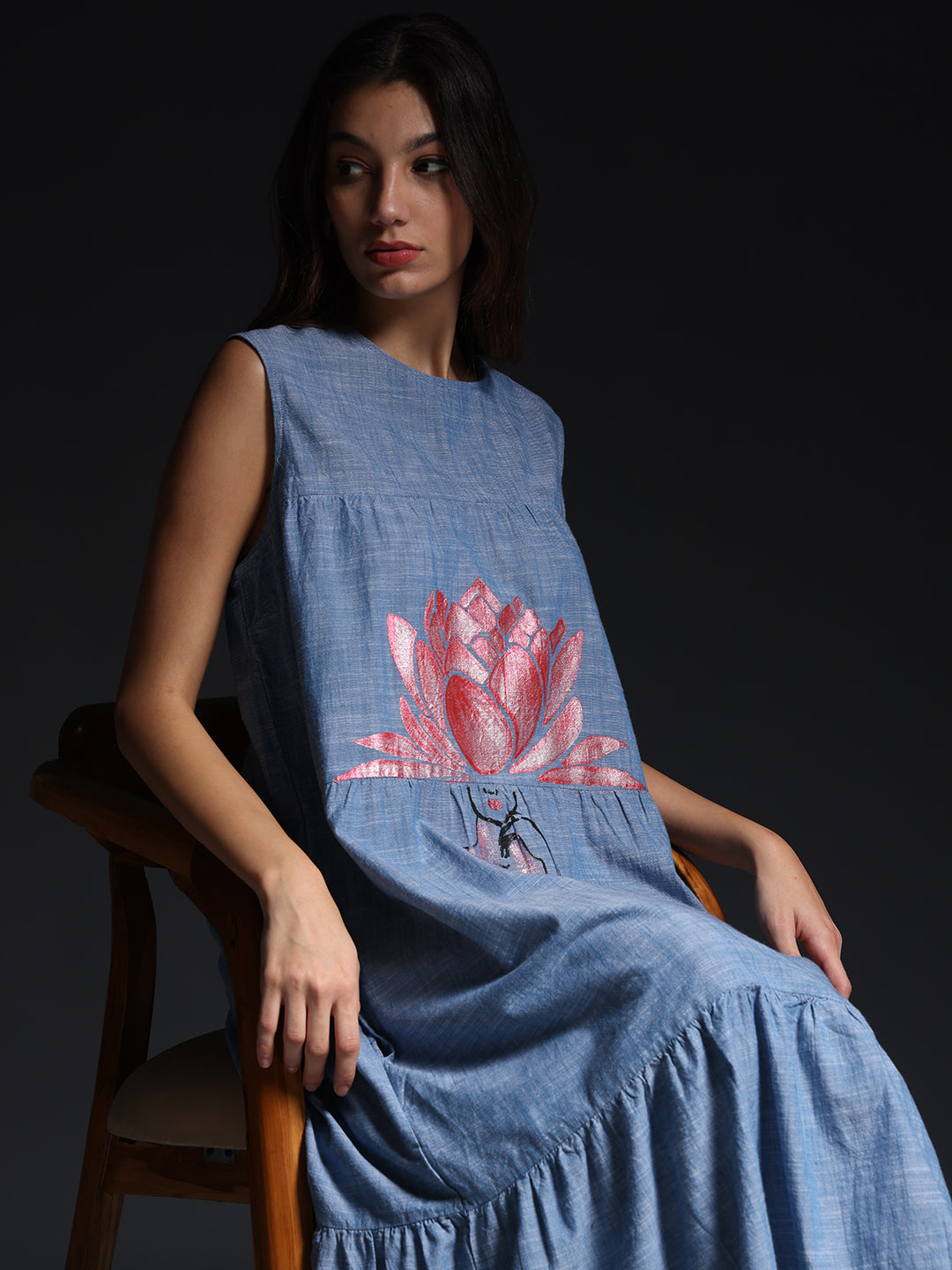 Gotamoda sleeveless maxi dress in blue with pink floral embroidery worn by model seated on chair