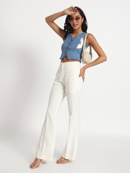 Woman wearing a sleeveless top in jeans with button details paired with white wide-leg pants and sunglasses