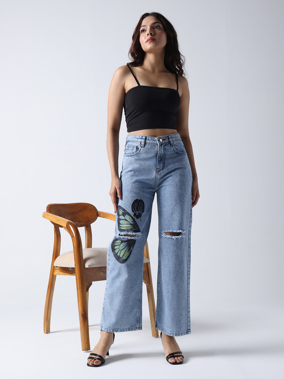 Gotamoda hand painted jeans with butterfly design worn by woman with black crop top and heels