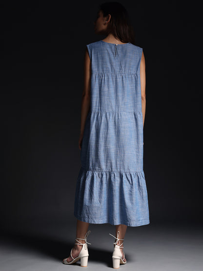Back view of model wearing Gotamoda blue sleeveless maxi dress with tiered design and white heeled sandals