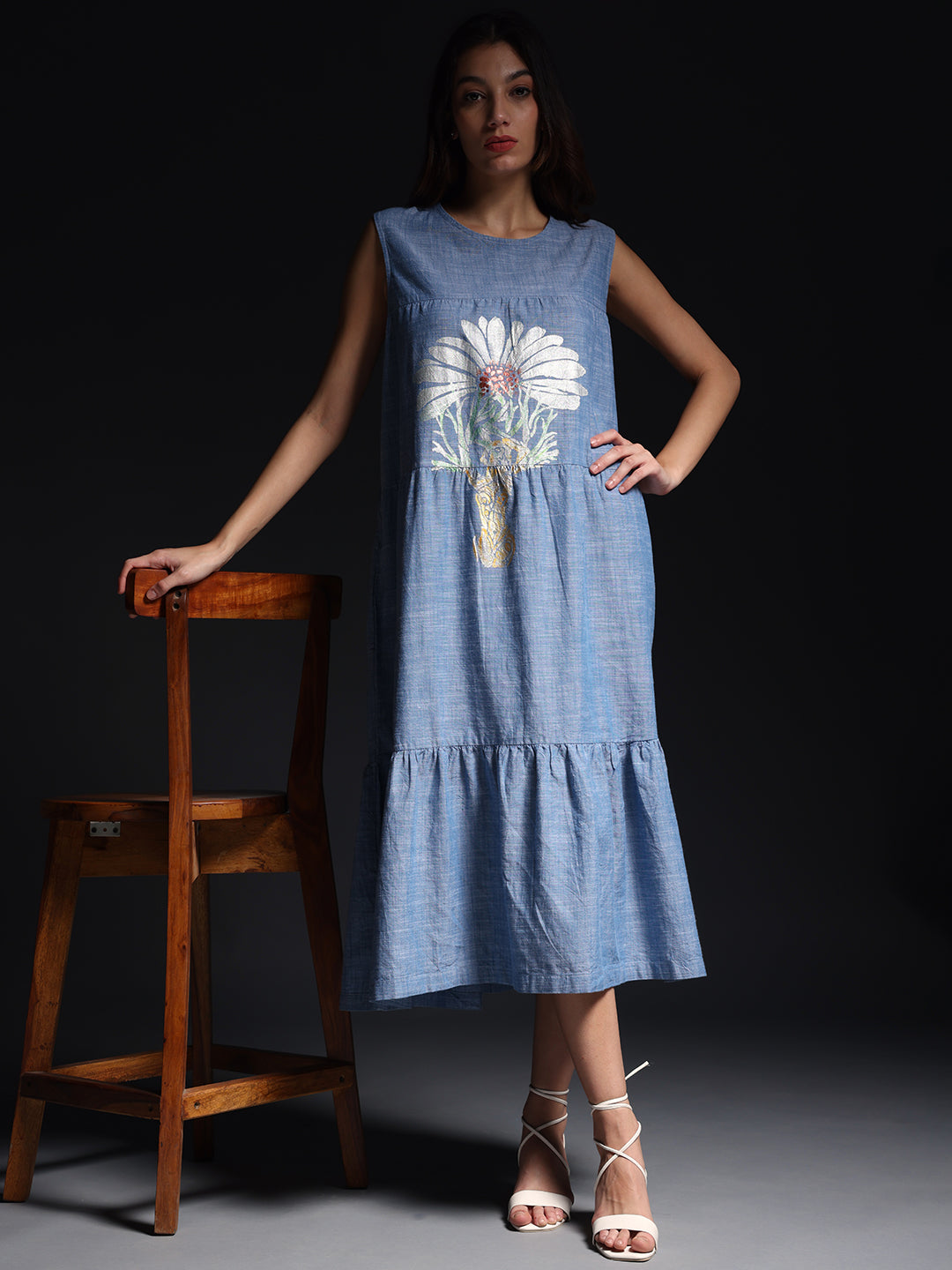 Gotamoda sleeveless maxi dress in blue with white floral print worn by model posing with wooden chair