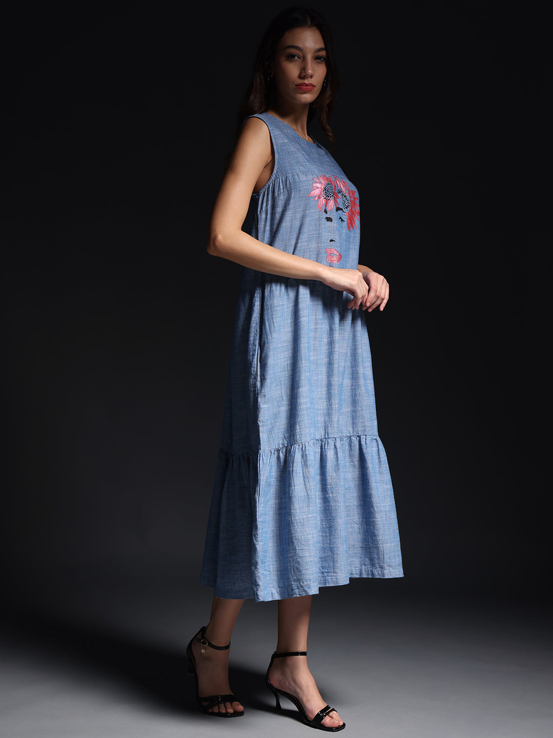 Woman wearing blue sleeveless maxi dress with floral print and ruffled hem paired with black heels